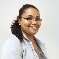 Aqueasha Martin-Hammond, a Black woman with long curly black hair, smiling, wearing a light gray blazer and dark gray shirt