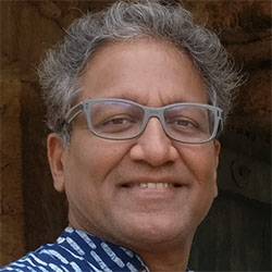 IMage of Manohar Swaminathan, a brown Asian indian man with grey hair, wearing spectacles and a blue striped shirt