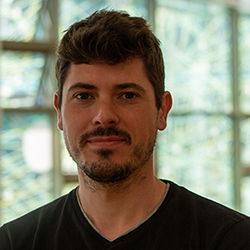 Hugo Nicolau, a white man with brown hair and dark blue shirt in front of glass windows