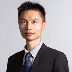 Mingming Fan, an asian man with black hair, smilng, wearing a black suit with a blue necktie, white background